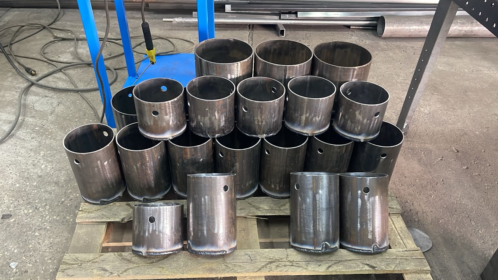 Металлические цилиндрические заготовки для вакуумных камер, выложенные на деревянный поддон в цехе.