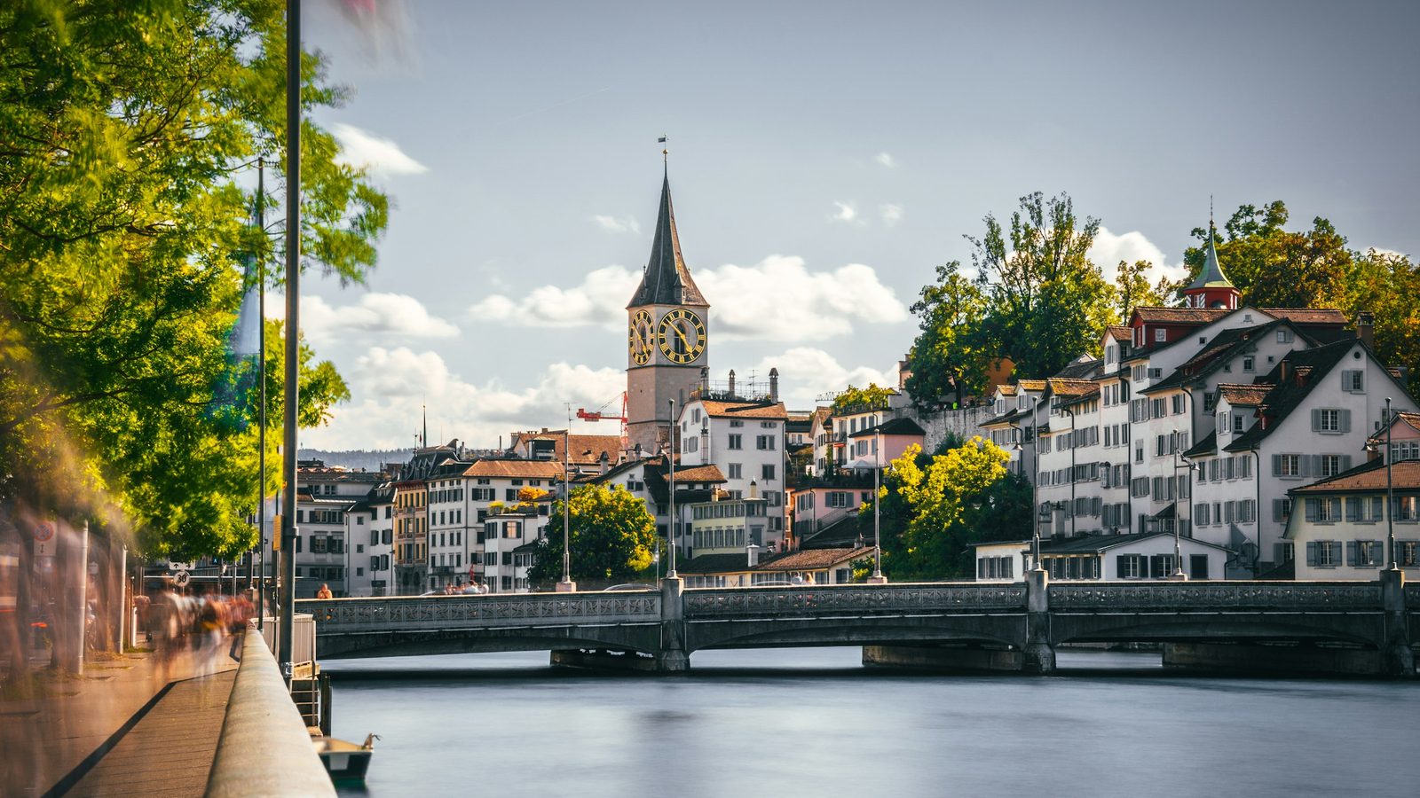 The Limmat river and a stone bridge in Zurich's old town, with the clock tower of St. Peter's Church behind the houses