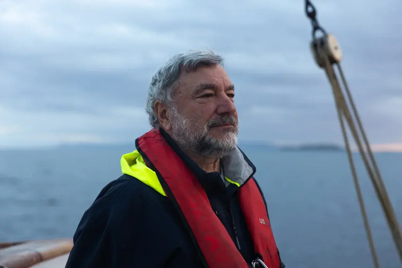 Experienced sailing captain aboard an expedition yacht, wearing a life jacket while navigating at sea. A professional polar expedition crew plays a key role in safely guiding small-group sailing voyages through the remote waters of Antarctica, Greenland and the Arctic.