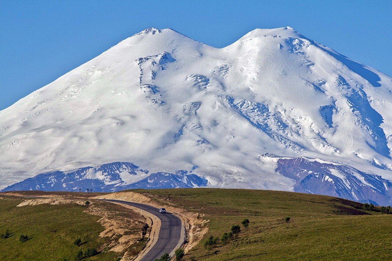 Snow-capped twin summits of Elbrus above green hills and a winding road