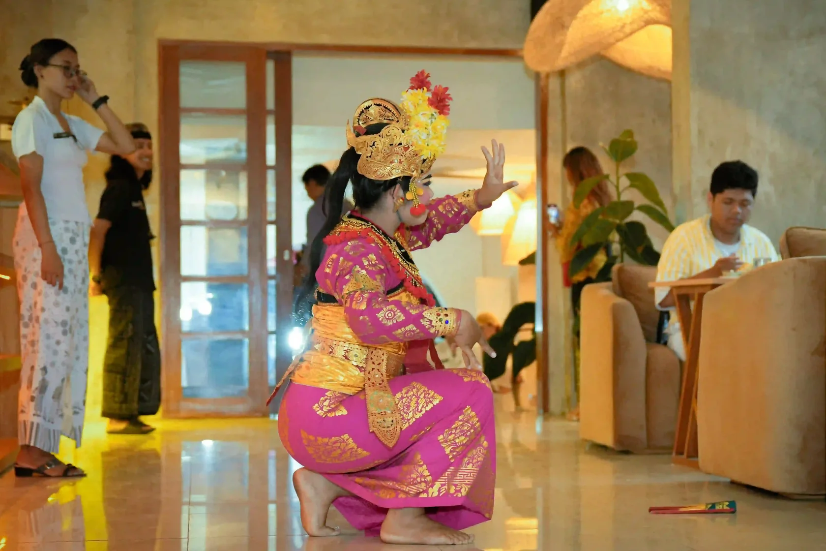 A captivated professional belly dancer in an intricate pink costume and traditional Balinese headdress performs a graceful routine on the floor of a modern cafe setting at Eden Ubud, while customers enjoy their meal nearby. This unique cultural experience is certainly the best event in Bali to see.