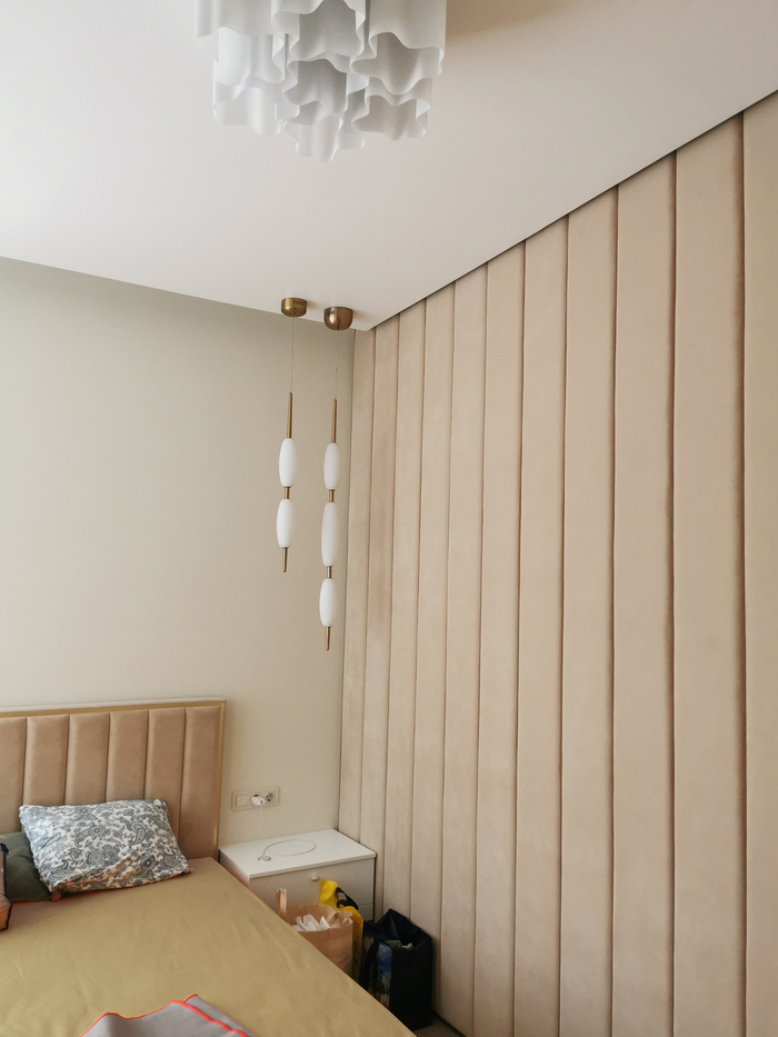 бежевая спальня с современным подвесным светильником, вертикальными мягкими стеновыми панелями