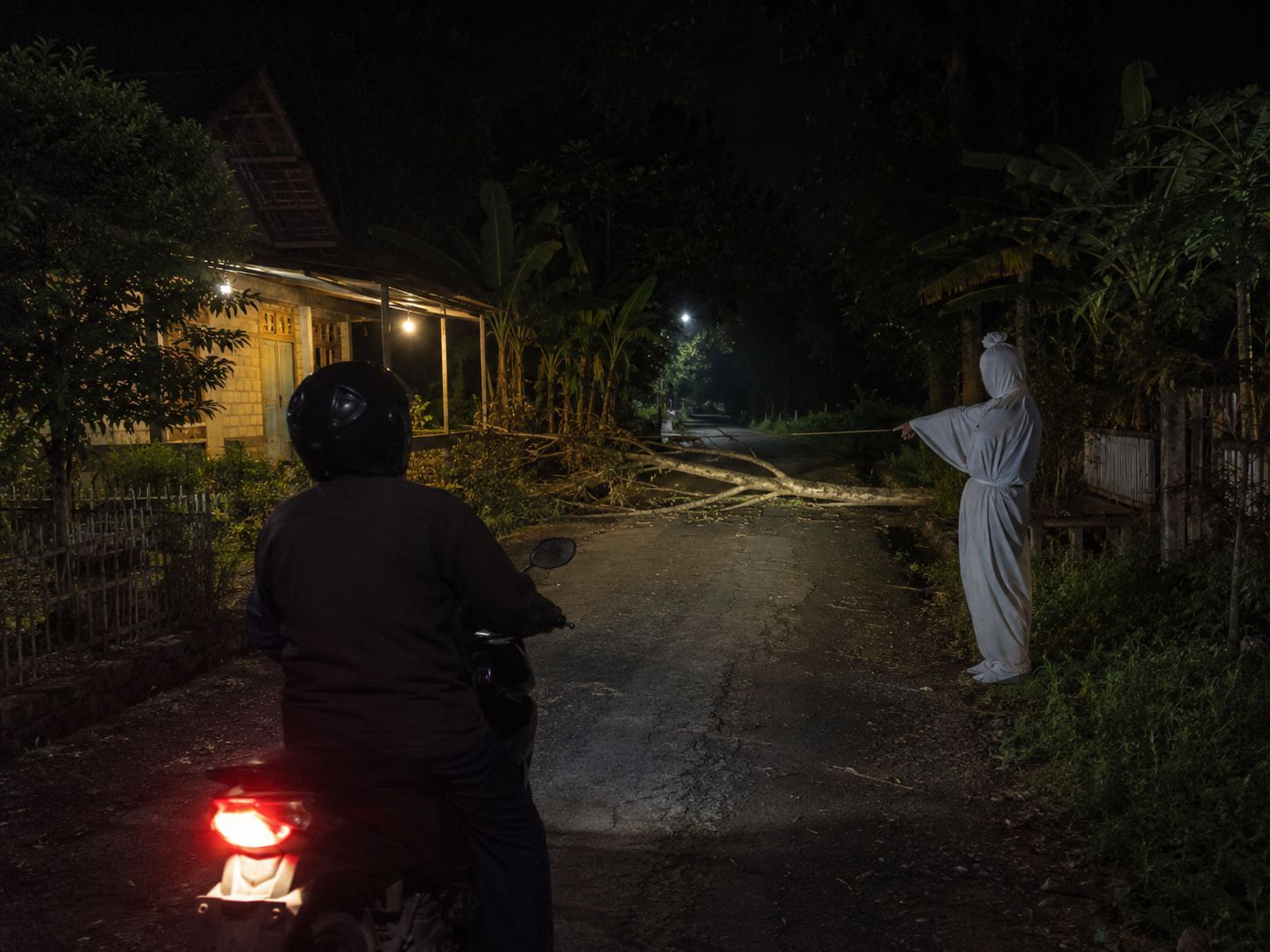 Pengendara motor berhenti saat sosok pocong memperingatkan adanya pohon tumbang di jalan kampung