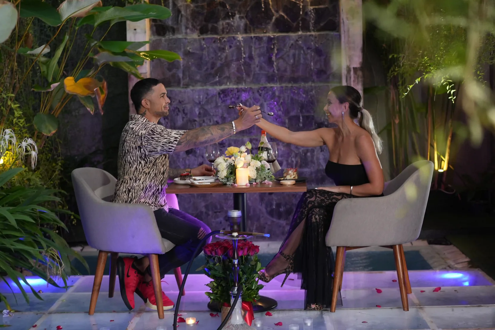 Romantic couple enjoying a shisha date with red roses and wine by the pool at Eden Hookah Club Bali.