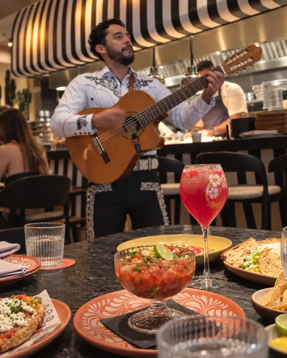 Brunch atmosphere visual: sharing plates and a pink drink with a guitarist in the background