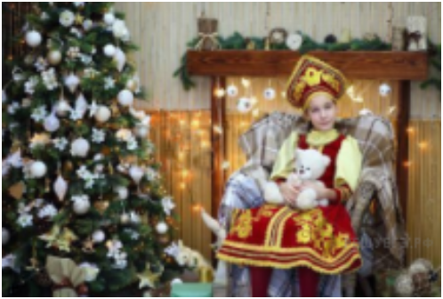 Фото 1. Описание. Девочка, одетая в традиционно русскую одежду, сидит в кресле у елки и держит мишку в руках