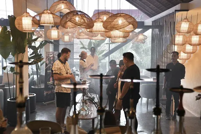 A group of friends gathering at a modern Eden Hookah Club location, featuring unique woven pendant lights and high-quality traditional pipes. Experience championship-level service at one of the best hookah bars in Bali.