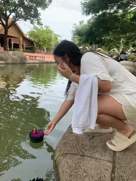 Девушка опускает кратонг на воду пруда