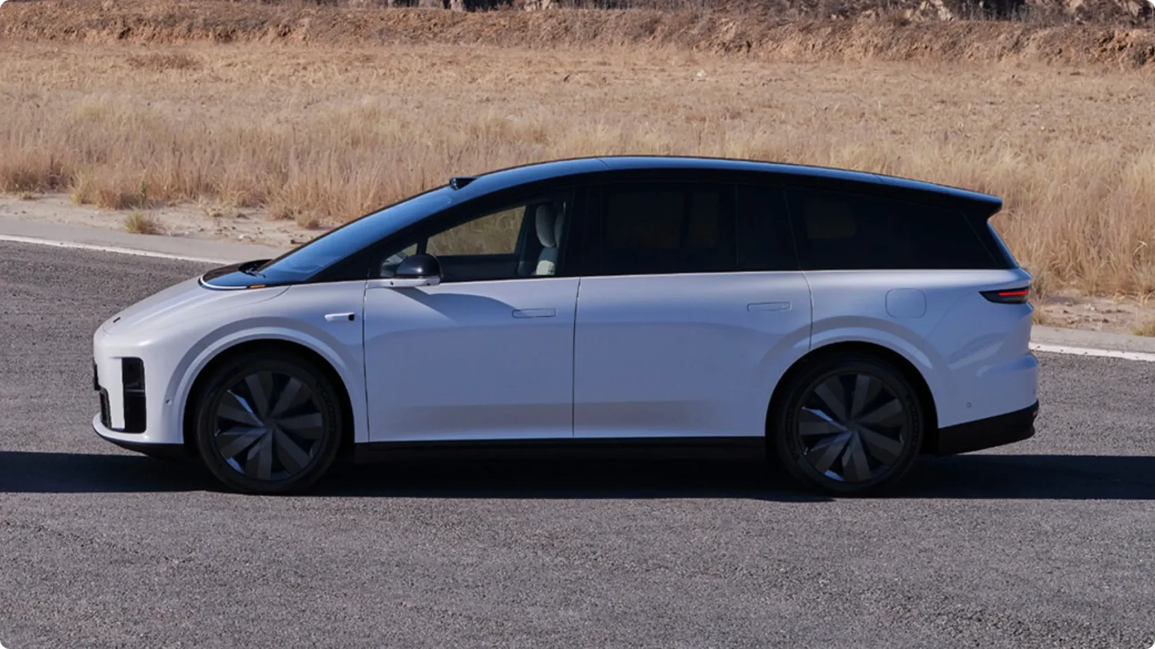 Боковой профиль электрического кроссовера Li Auto i8 в белом цвете с черной крышей, припаркованного на дороге в пустынной местности, вид на аэродинамические диски и утопленные дверные ручки.