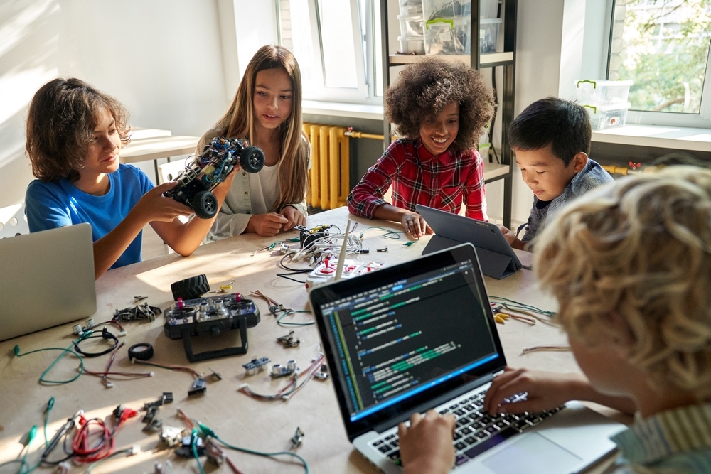 Children sat around a table building electric models and coding them on their laptops