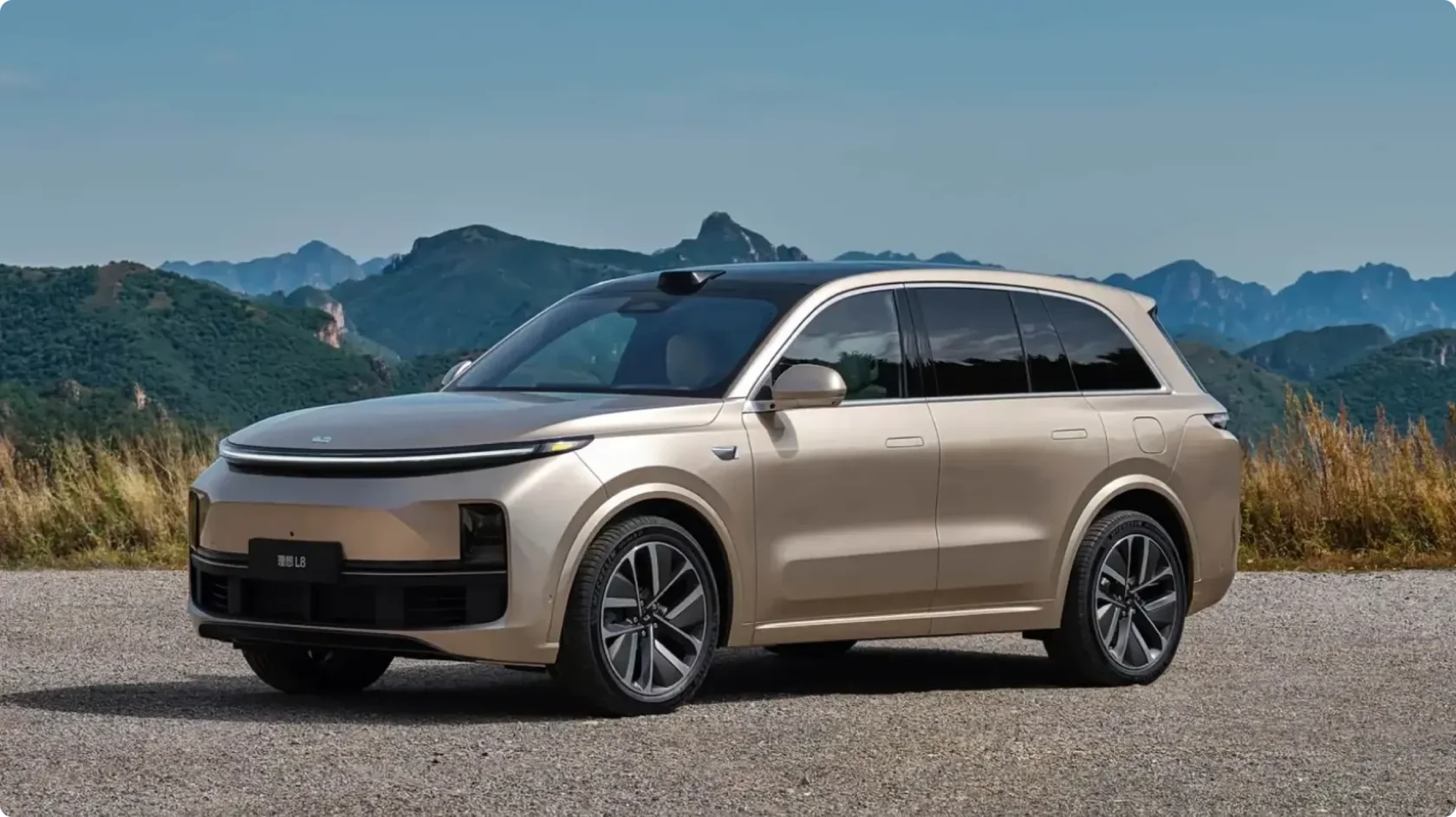 Текущее поколение гибридного кроссовера Li Auto L8 в золотисто-бежевом цвете на фоне горного пейзажа, вид спереди сбоку: светодиодная полоса, лидар на крыше и утопленные дверные ручки