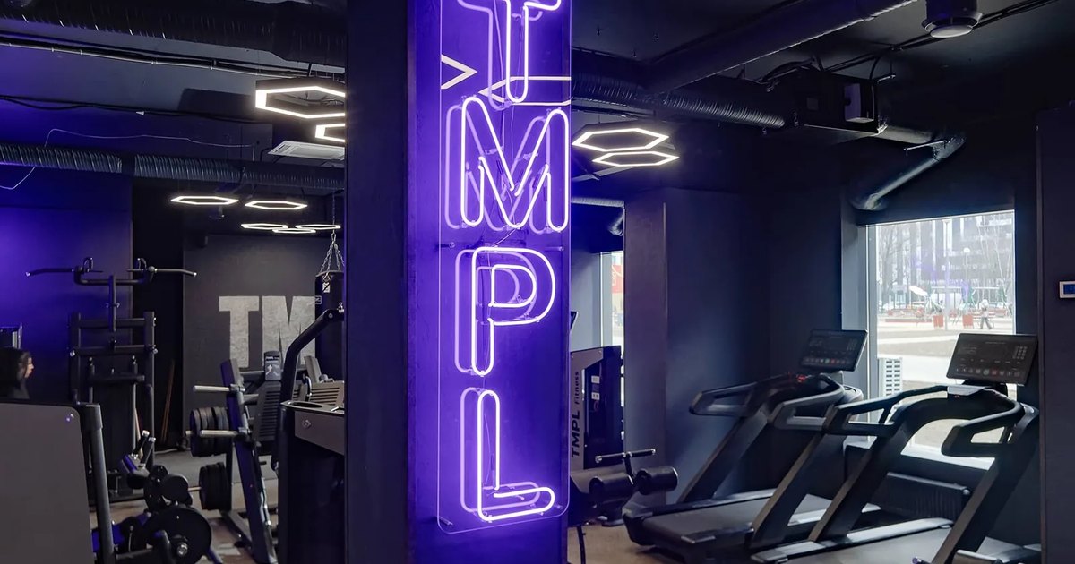 Неоновая вывеска TMPL Fitness на колонне в зале клуба беговые дорожки у панорамного окна