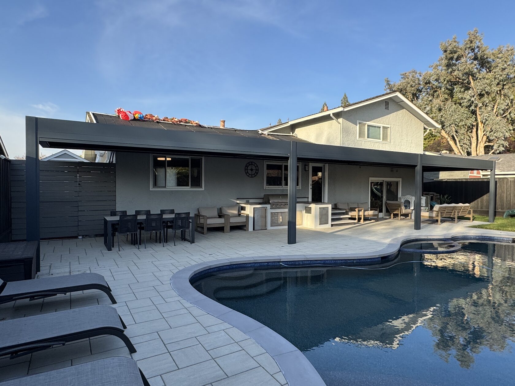 Large attached aluminum pergola covering a poolside patio and outdoor kitchen