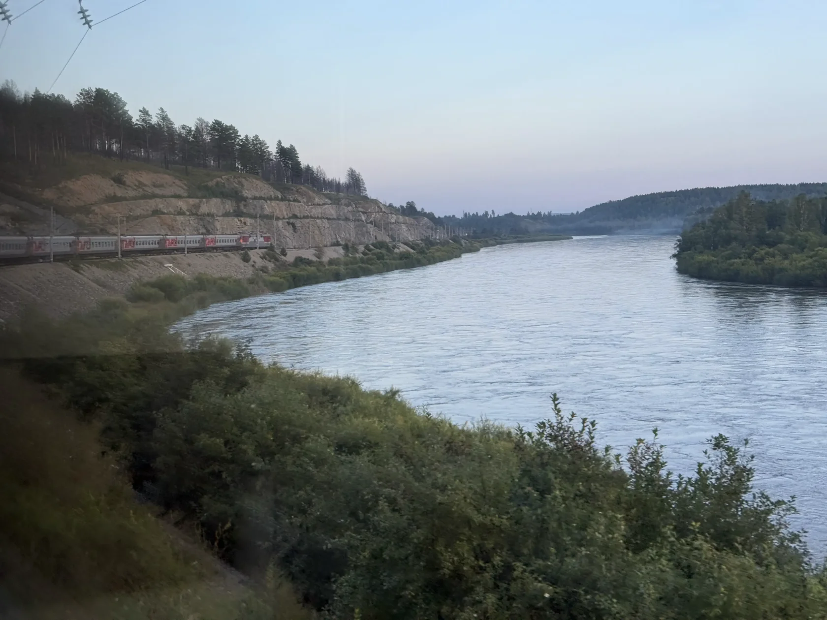 Поезд идет по повороту вдоль широкой реки Ингода