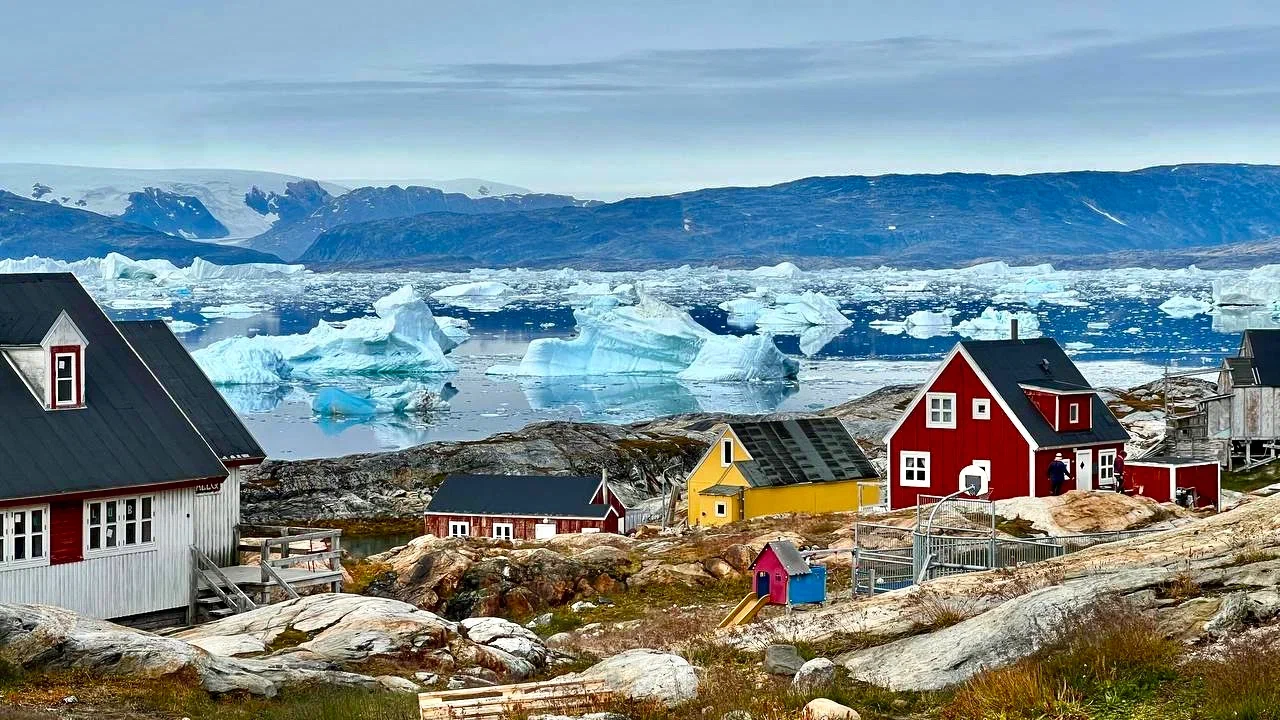 Colorful houses in a traditional Greenland village overlooking an iceberg-filled fjord and Arctic mountains