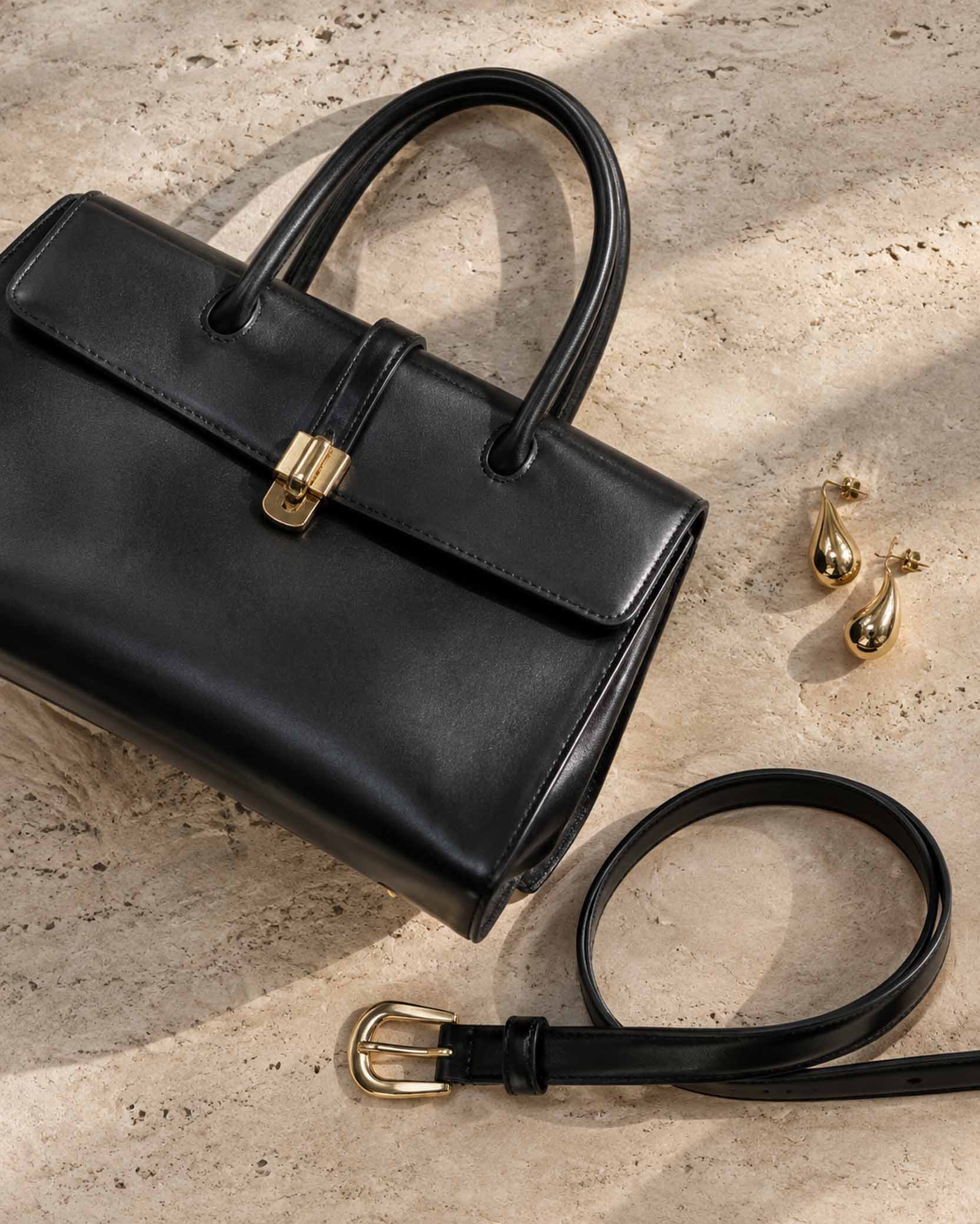 черная кожаная сумка, ремень и золотистые серьги на светлом фоне.