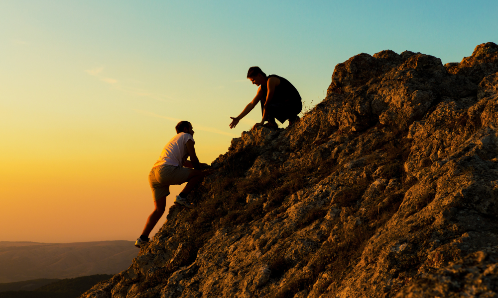 two men climbing a mountain, with the one helping the other to get higher, like safeguarding, you can&amp;#39;t do things alone