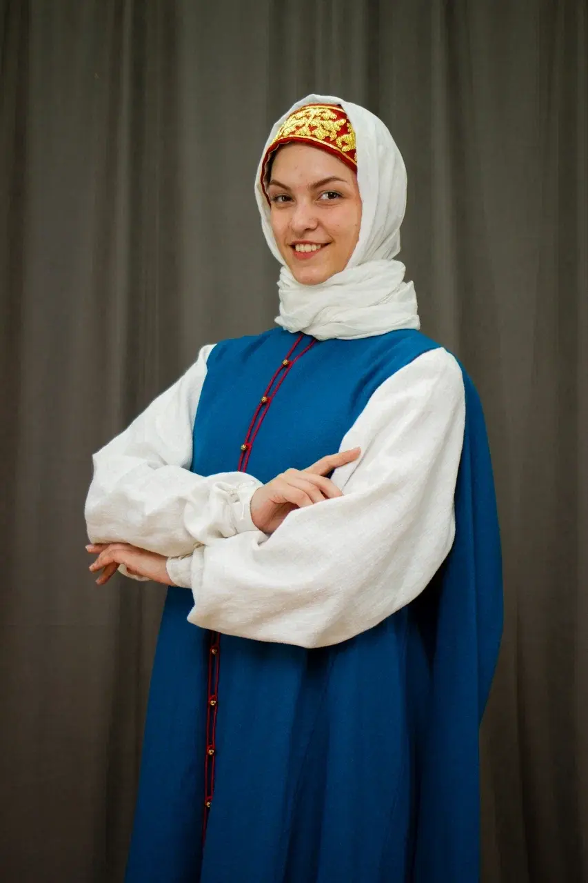 Woman in a traditional blue sarafan, white blouse and headscarf smiling