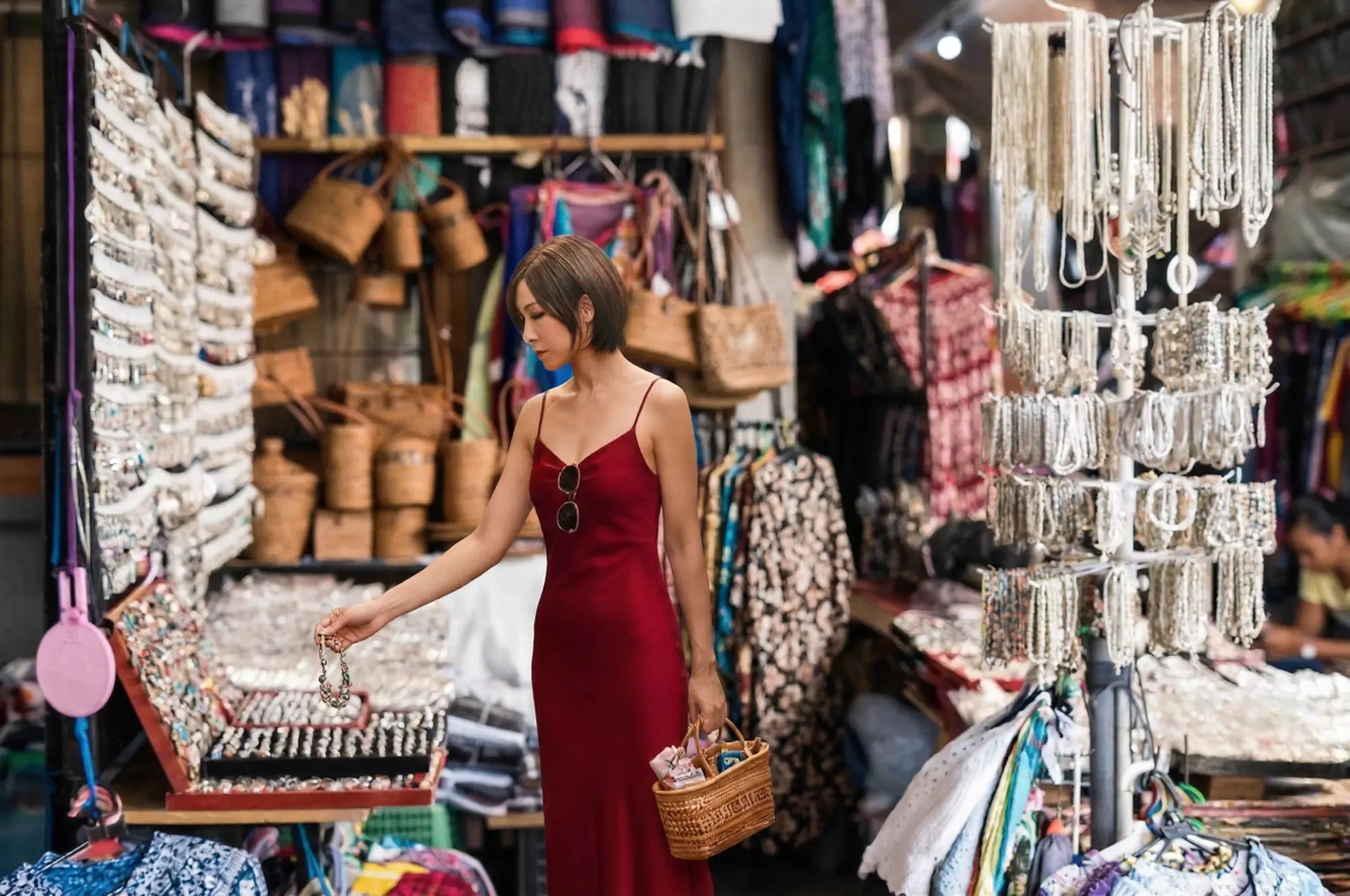 A woman carefully examining a display of traditional silver rings and bracelets at a bustling indoor vendor stall within the Ubud Art Market.