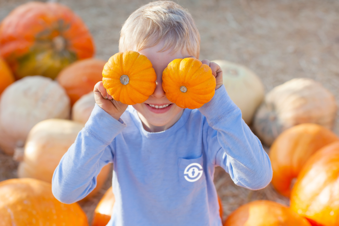 A child holding 2 small pumpkins up to their face like they're their eyes