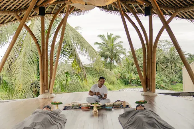 A practitioner performing a serene sound healing session with singing bowls for two guests under a bamboo canopy at Hammana Spa, known as one of the best spa in Ubud experiences.