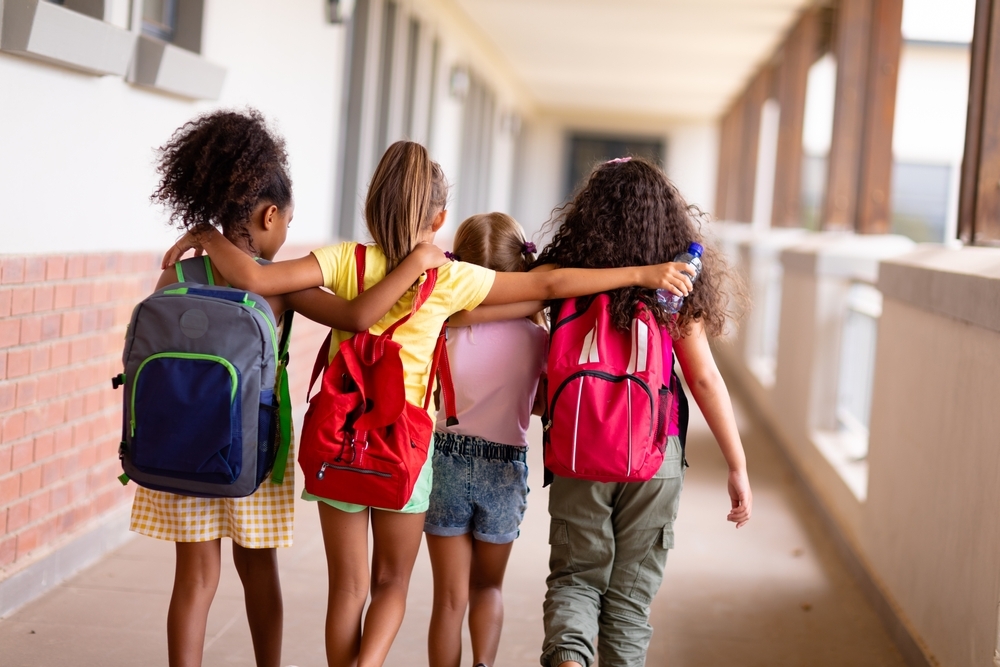 Four mixed ethnicity girls walking down a school corridor away from the camera