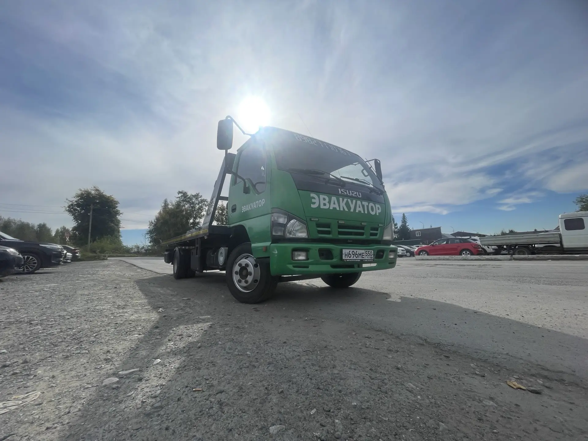 Эвакуатор Isuzu едет по асфальту в солнечную погоду, вид сбоку