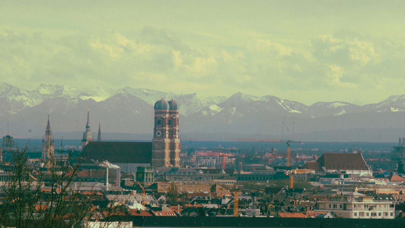 Munich's skyline with the twin domed towers of the Frauenkirche, church spires and red roofs, and the snow-capped Alps behind