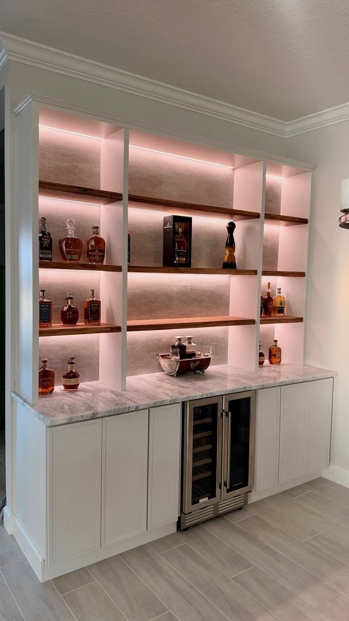 Completed Tampa home bar featuring illuminated solid wood display shelves, painted base cabinets, beverage refrigeration, and a light stone countertop
