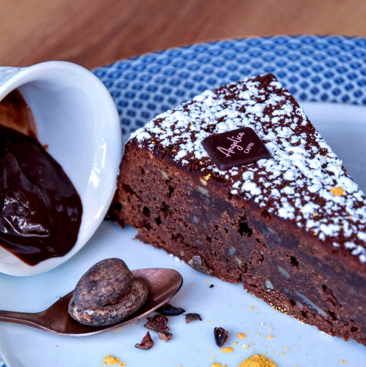 Треугольный кусок торта Капрезе от Pasticceria Angelica с шоколадным соусом и цельными какао-бобами на тарелке