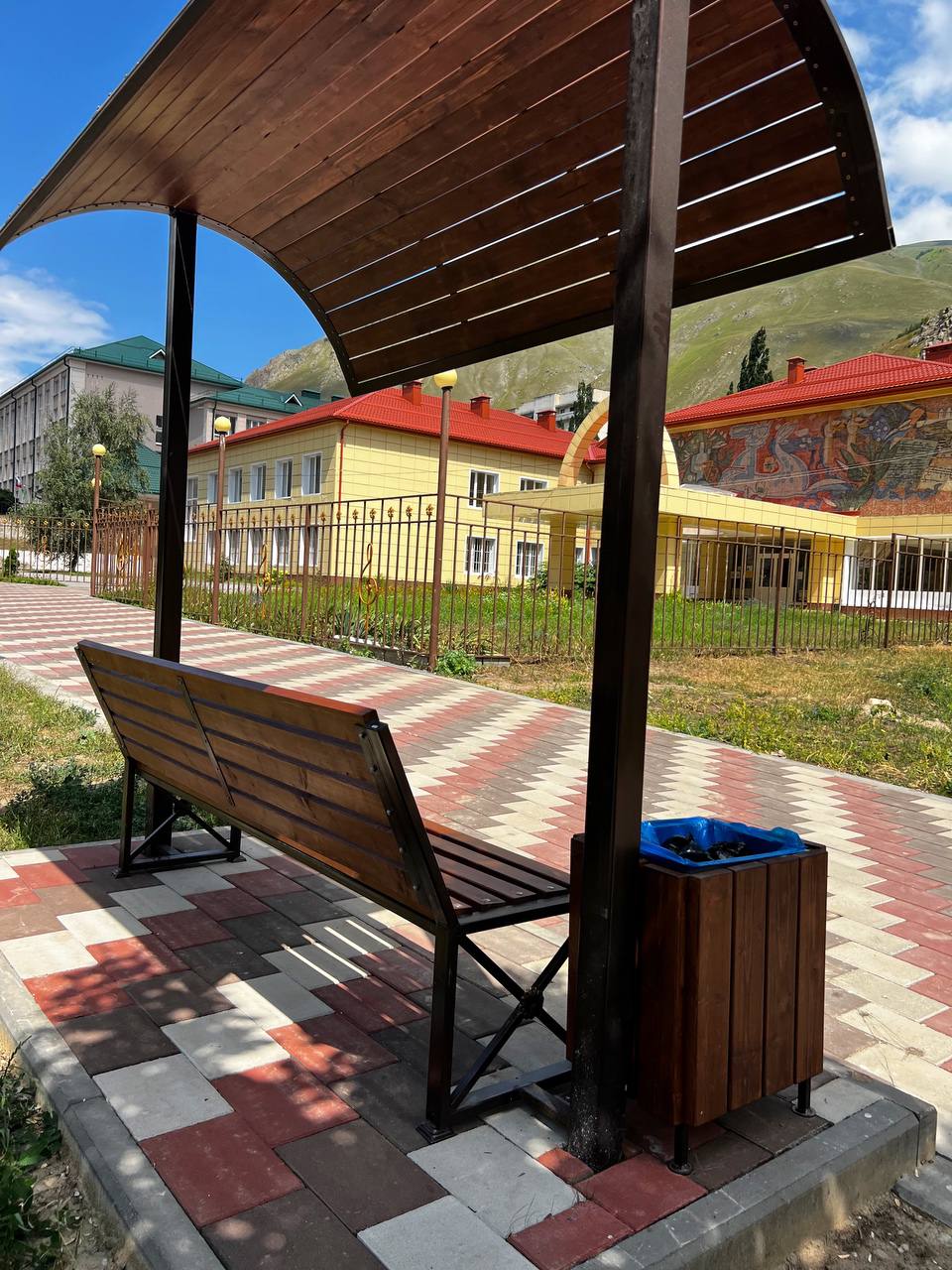 Скамейка под навесом с урной рядом с прогулочной дорожкой