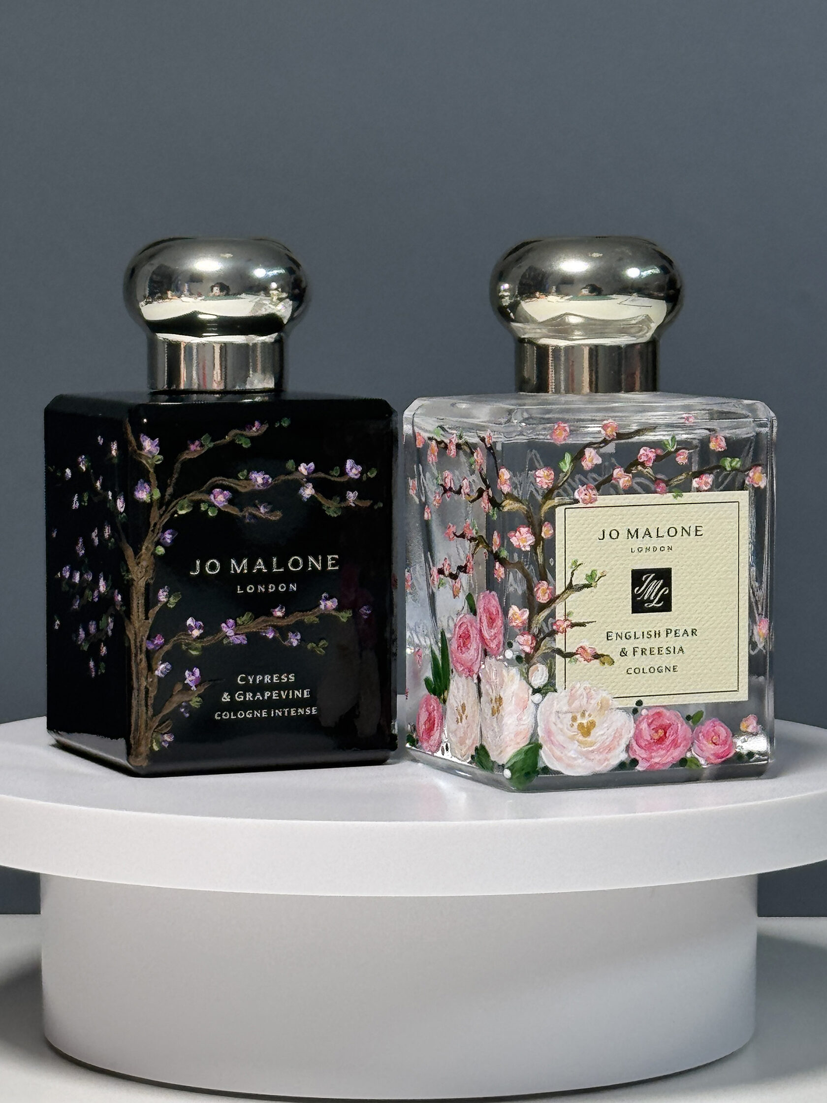 Pair of custom hand-painted Jo Malone perfume bottles with cherry blossom and dark floral artwork by Julia Razz.