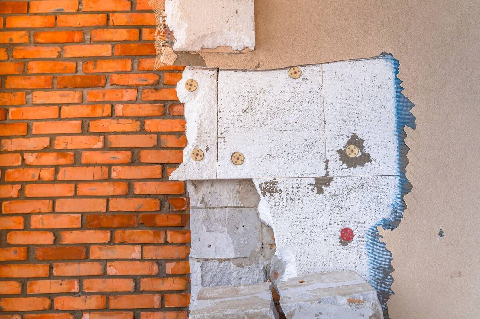 Разобранный фасад частично очищен до кирпича и старого утеплителя. Видны слои мокрого фасада, демонтированные покрытия и крепежи, пример очистки слабых участков перед ремонтом.