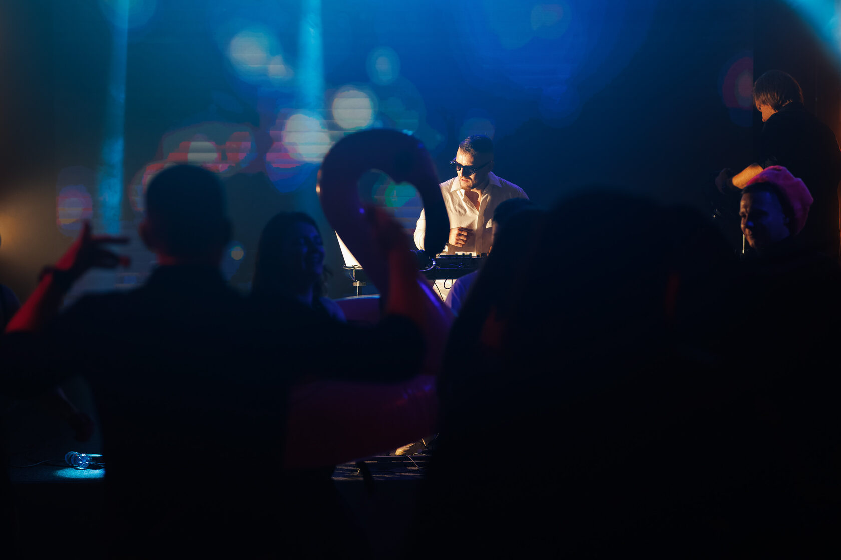 Гости перед сценой в синем свете наблюдают за DJ ROZHKOV, работающим за диджейским пультом.
