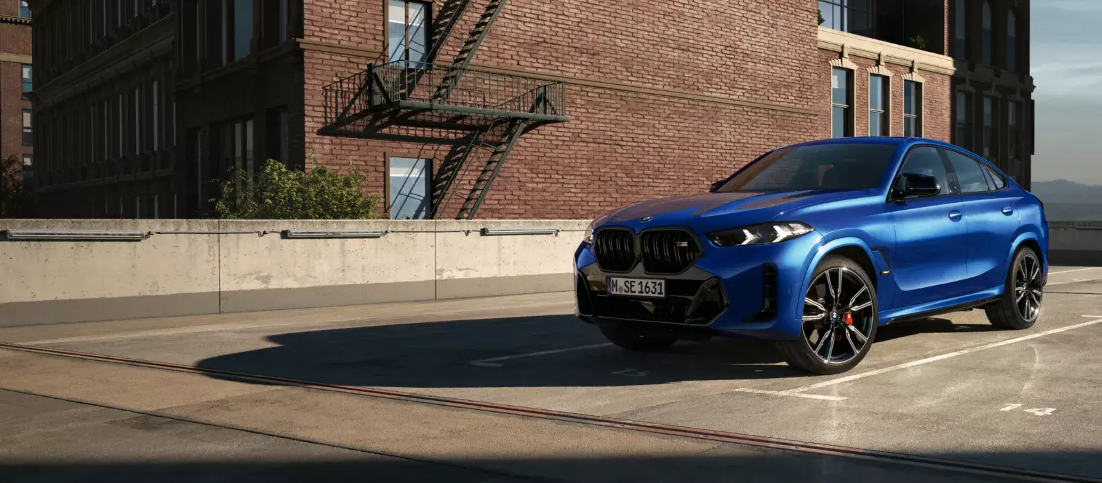 BMW X6 стоит на солнце на парковке перед кирпичной стеной