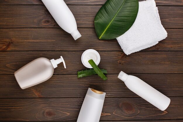 Бесплатное фото Белое полотенце, бутылки шампуня и кондиционера лежат на столе с зеленым листом и алоэ