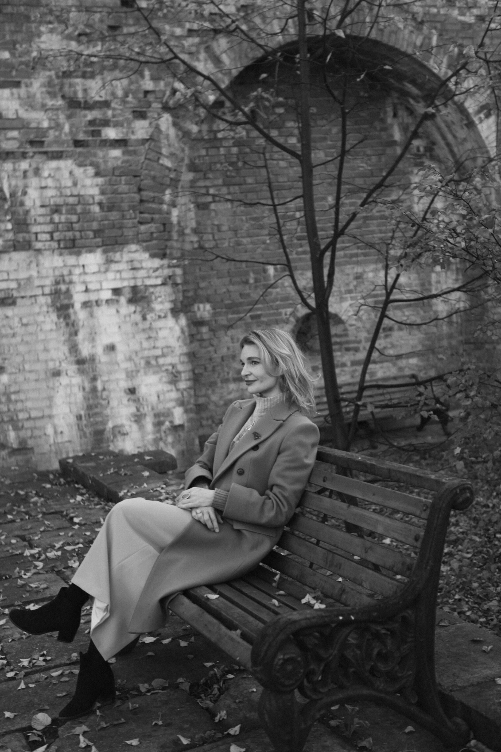 Natalia — founder, photographed in black and white on a bench beneath a brick arch