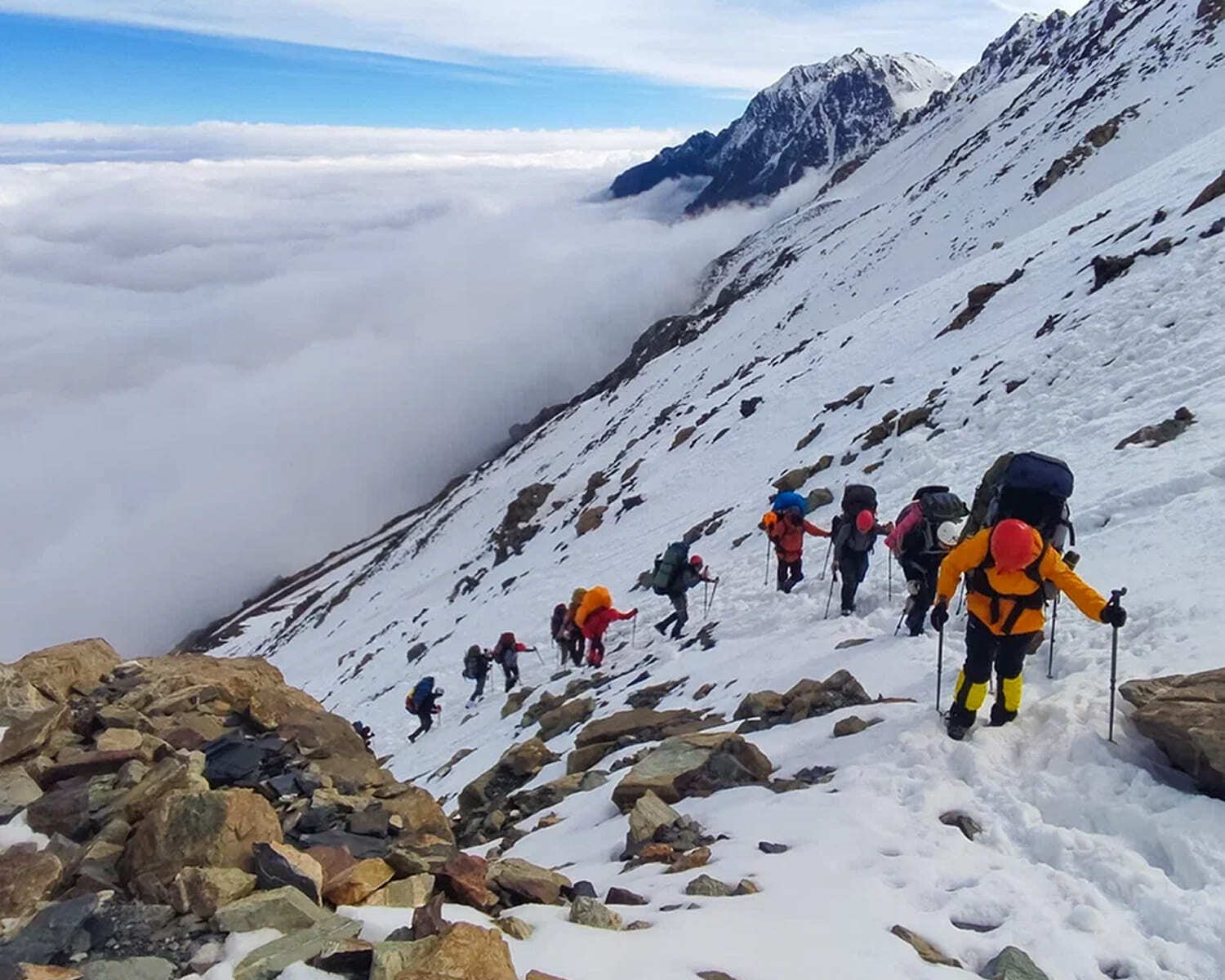 Roped climbers on a steep snow slope above a sea of clouds