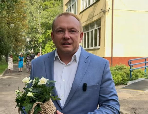 Мужчина с букетом роз в руках стоит на улице возле школы