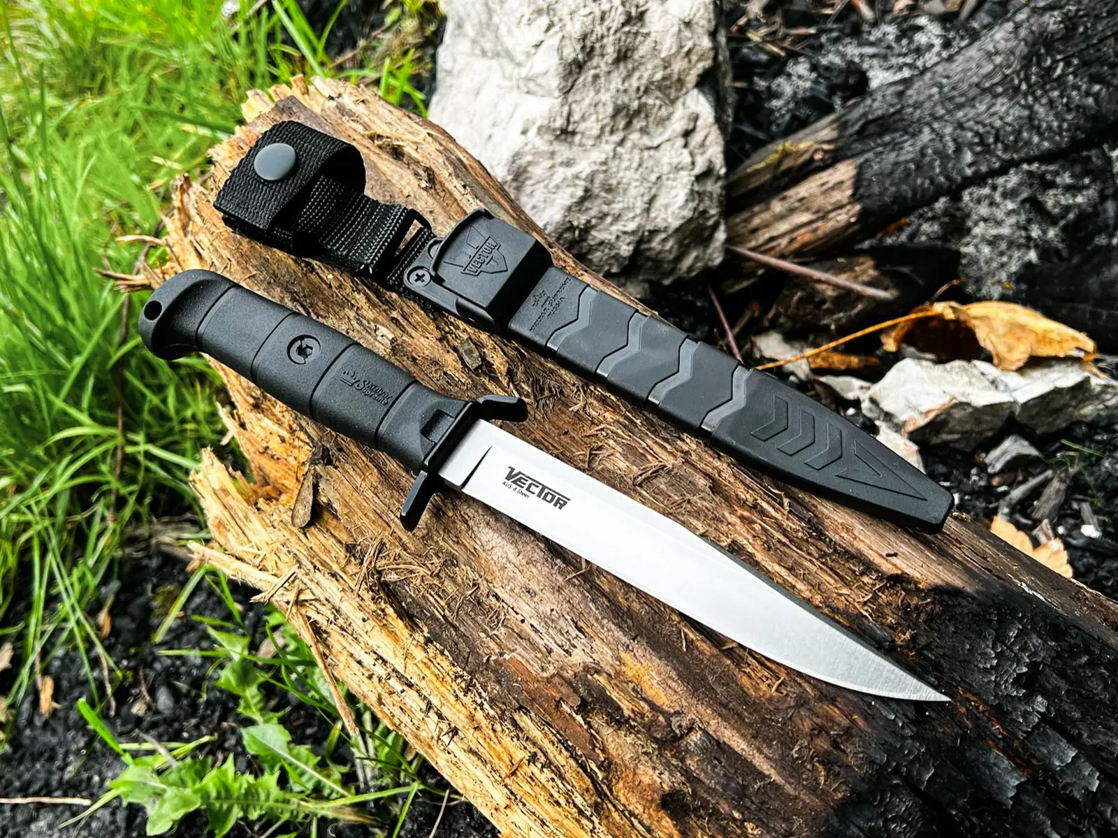 Black Kizlyar Supreme Vector and sheath shown across a charred log