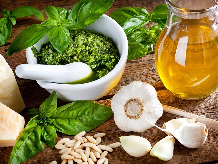 Bowl of homemade organic pesto with fresh basil, garlic cloves, pine nuts, and olive oil on a wooden surface, highlighting natural ingredients for pest control solutions in gardening.