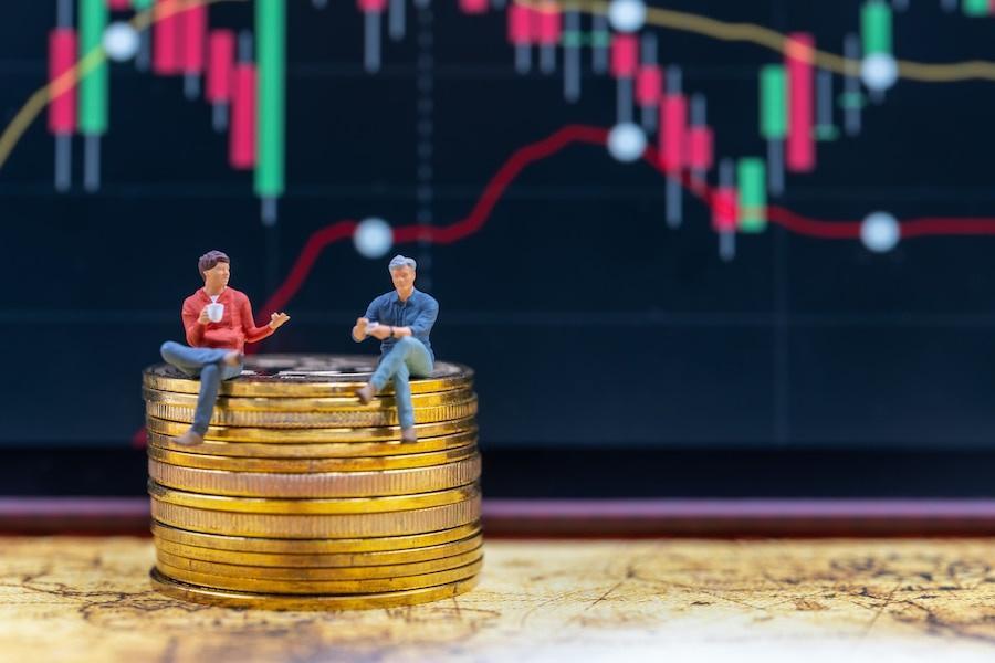 Bitget Leverage Trading: two businessman miniature figure sitting on stack of gold Bitcoin coins with candlestick chart 