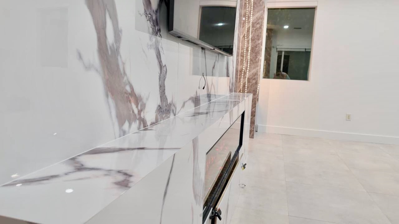 Side detail of a custom marble-look media wall showing the integrated linear electric fireplace and polished architectural surround.