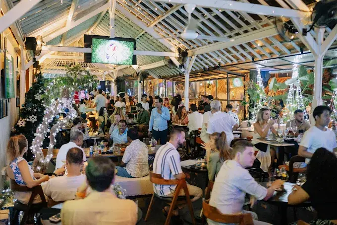 A lively and welcoming crowd socializing under glowing string lights at The Blue Door's beer garden, a vibrant choice for where to go after dinner in Bali.