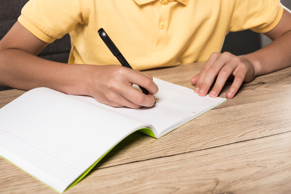 He is writing. Блокнот для домашнего задания. Стол для домашней работы пустой.