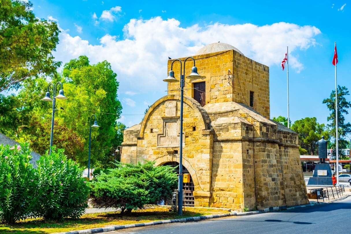 Киренийские ворота — каменное здание с куполом и арочным входом, окружённое зеленью.