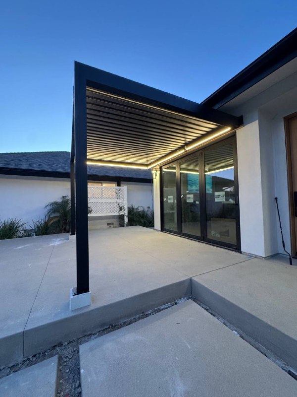 Wide blue-hour view of the illuminated black pergola above the concrete patio.
