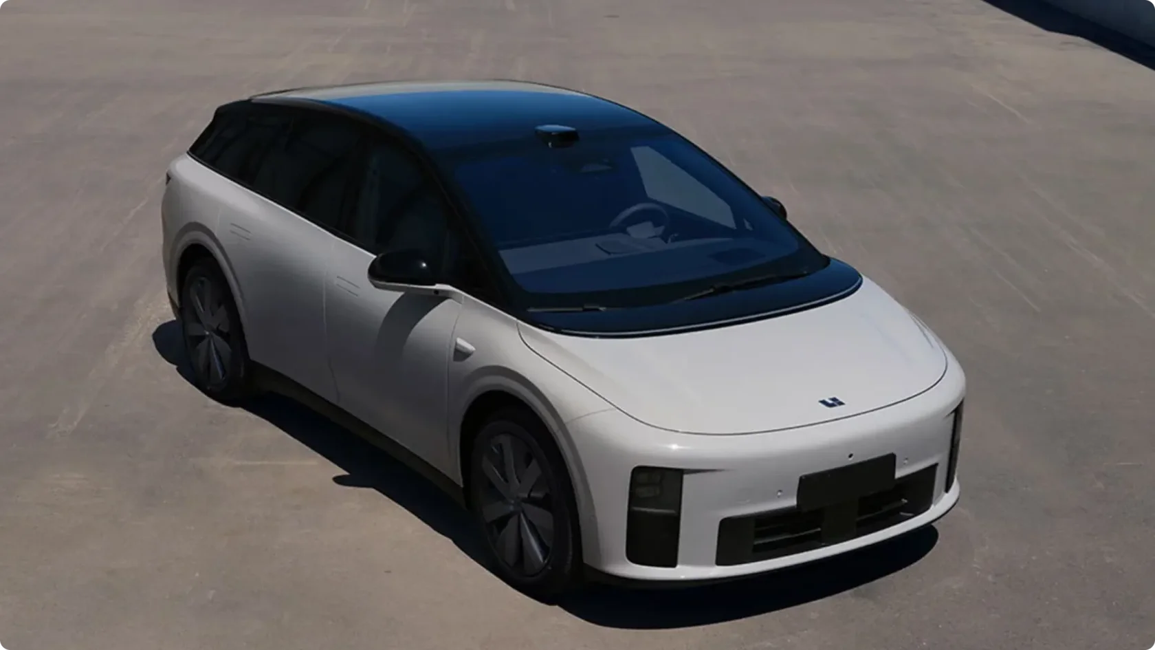 Электрический внедорожник Li Auto i8 в белом цвете с черной крышей, вид сверху сбоку на асфальтированной площадке: аэродинамичный профиль, лидар на крыше и утопленные дверные ручки.