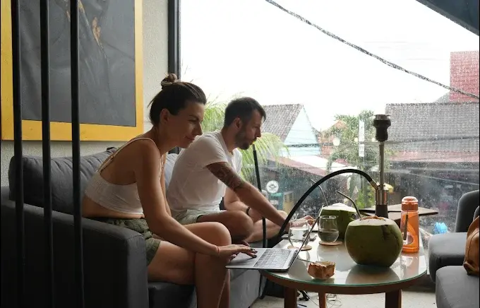 A couple working productively on their laptop by the window with fresh coconuts and a hookah at the Eden Canggu venue, recognized as the best coworking space in Bali.