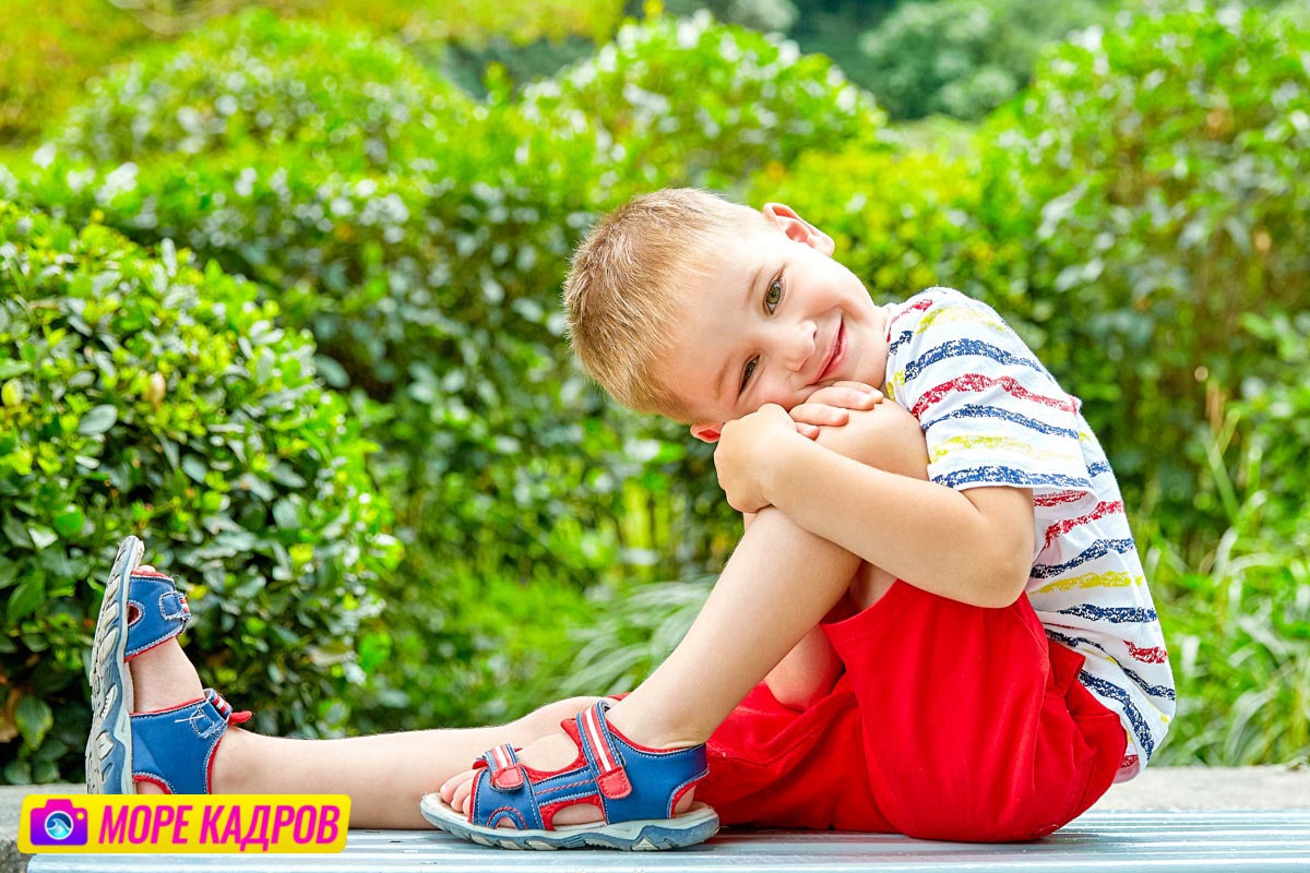 мальчик в красных шортах сидит на фоне зелени, портрет ребенка 